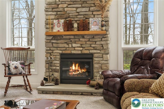 living area featuring baseboards, a stone fireplace, and carpet