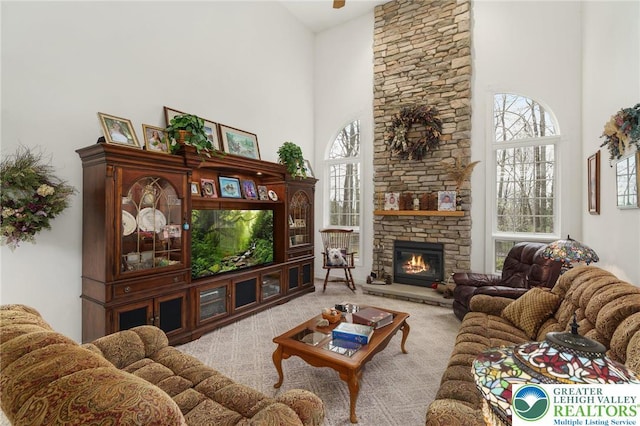 living area with a stone fireplace, carpet, and a high ceiling