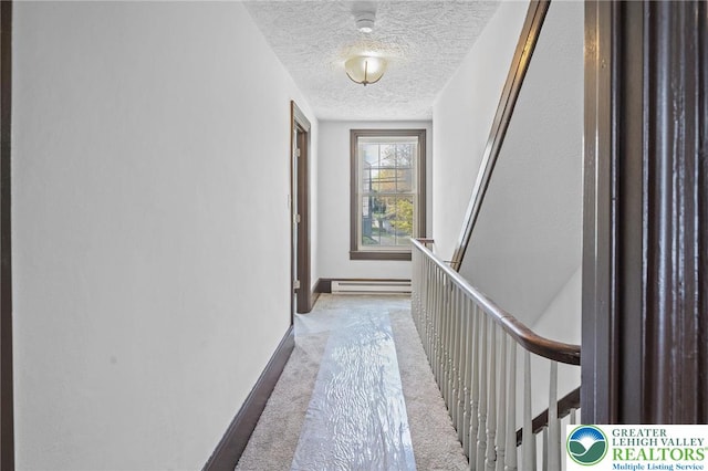 corridor with carpet floors, baseboards, a textured ceiling, a baseboard heating unit, and an upstairs landing