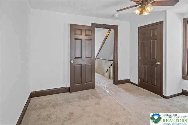 unfurnished bedroom featuring carpet floors, a textured ceiling, baseboards, and a ceiling fan