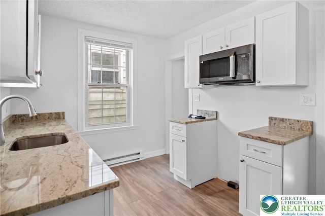 kitchen featuring light wood-style floors, baseboard heating, white cabinets, light stone counters, and a sink