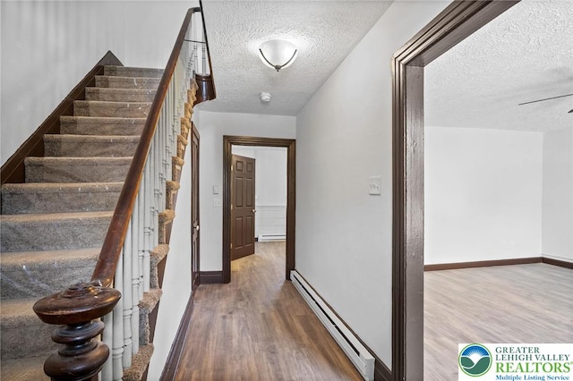 hall with baseboard heating, a textured ceiling, baseboards, wood finished floors, and stairway