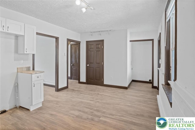 interior space with light wood-style floors, track lighting, baseboards, and a textured ceiling