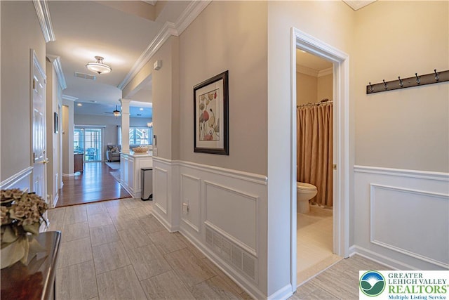 corridor with crown molding, a decorative wall, and visible vents