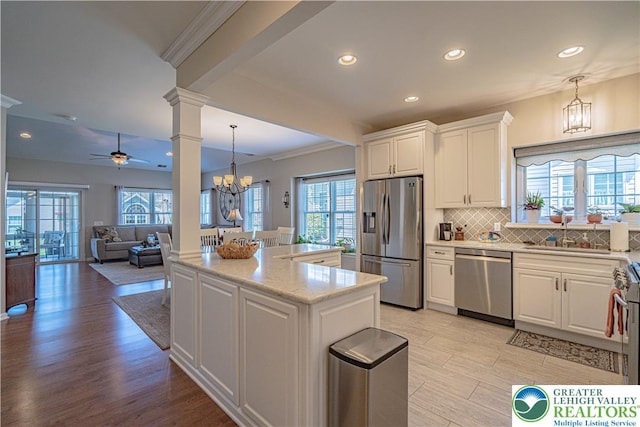 kitchen featuring a sink, ceiling fan with notable chandelier, stainless steel appliances, white cabinetry, and decorative columns