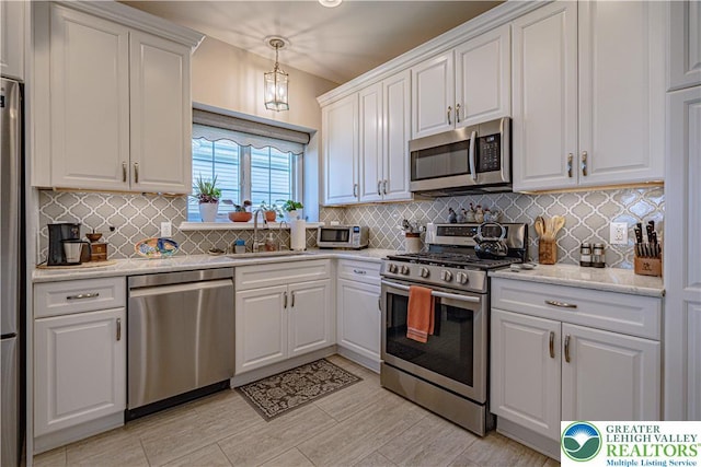 kitchen with decorative backsplash, hanging light fixtures, a sink, stainless steel appliances, and white cabinetry