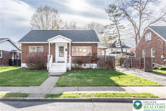 bungalow with brick siding, fence, a shingled roof, and a front lawn