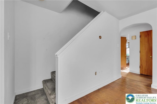 empty room with baseboards, arched walkways, stairs, and wood finished floors