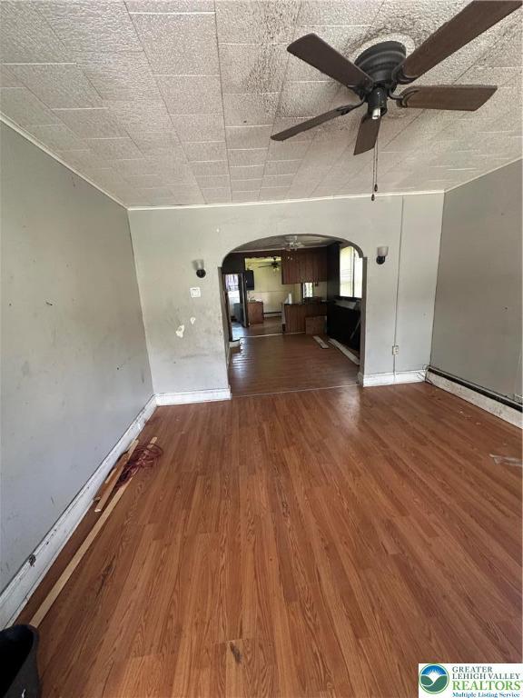 unfurnished living room featuring arched walkways, ceiling fan, baseboards, and wood finished floors