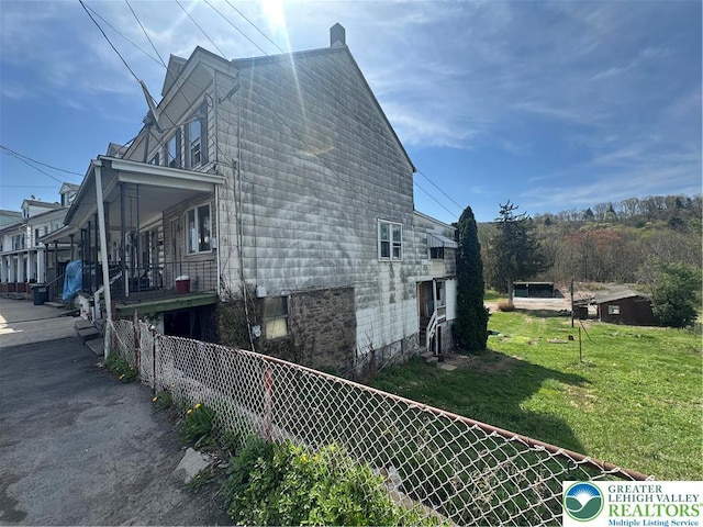 view of side of home featuring fence, a chimney, and a yard