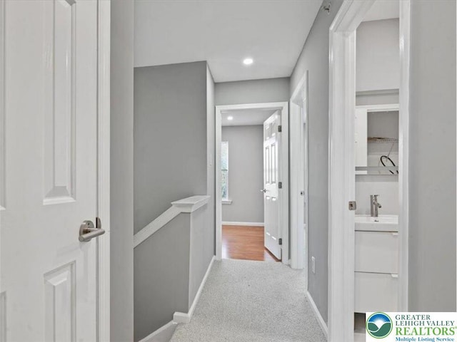hallway with carpet floors, baseboards, recessed lighting, a sink, and an upstairs landing