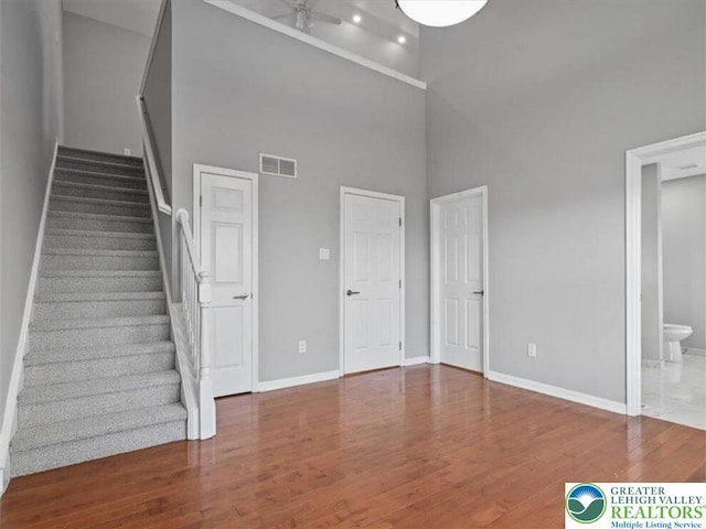 staircase with baseboards, a high ceiling, ceiling fan, and wood finished floors
