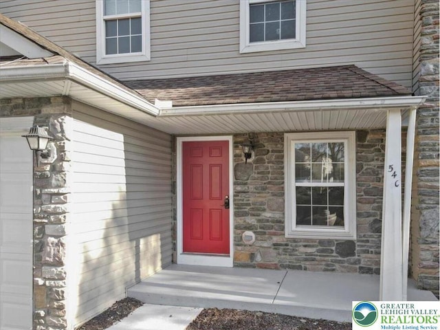 doorway to property with a garage, a shingled roof, and stone siding