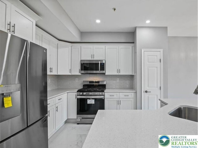 kitchen featuring white cabinetry, appliances with stainless steel finishes, a sink, and marble finish floor