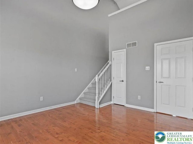 interior space featuring a towering ceiling, visible vents, wood finished floors, baseboards, and stairs