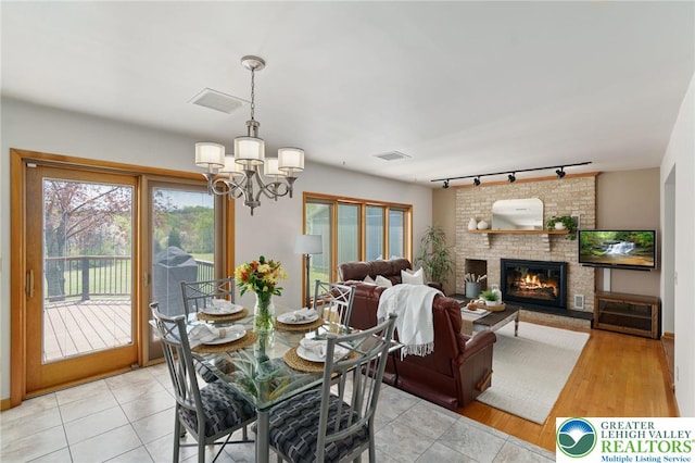 dining room featuring track lighting, a brick fireplace, a chandelier, and visible vents