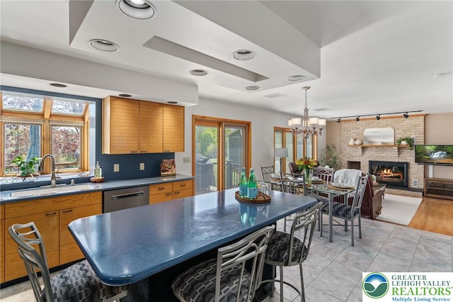 kitchen featuring a fireplace, brown cabinets, dishwasher, a sink, and track lighting