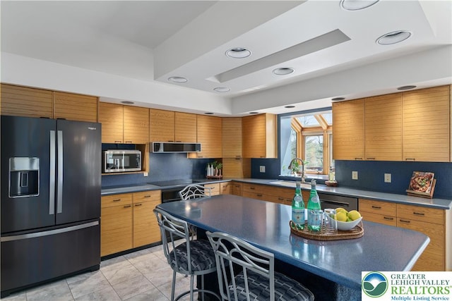 kitchen with appliances with stainless steel finishes, tasteful backsplash, dark countertops, a sink, and a breakfast bar
