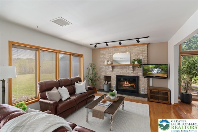 living room with a fireplace, rail lighting, wood finished floors, and visible vents