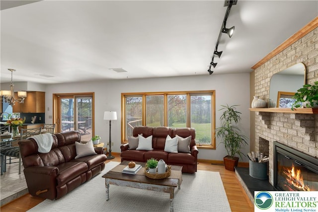 living area with a fireplace, rail lighting, wood finished floors, baseboards, and a notable chandelier