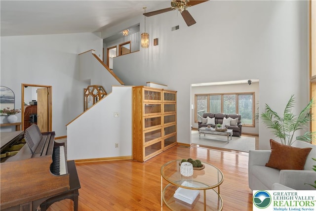 living area with stairs, a ceiling fan, high vaulted ceiling, and wood finished floors