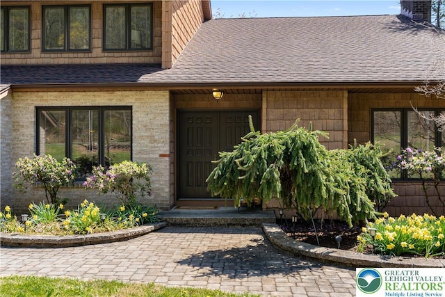 view of exterior entry with a shingled roof and a chimney
