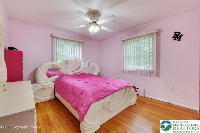 bedroom with ceiling fan, a baseboard heating unit, baseboards, and light wood-style floors