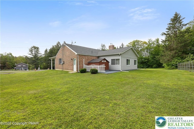 rear view of property with a lawn, brick siding, a chimney, and a patio