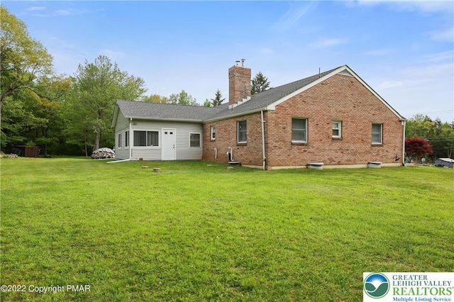 back of property with brick siding, a yard, and a chimney