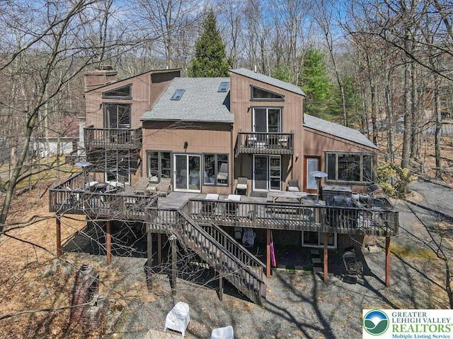 back of property featuring roof with shingles, stairs, a chimney, and a balcony