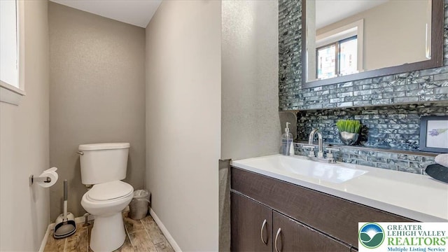 half bath featuring toilet, baseboards, decorative backsplash, and vanity