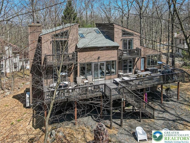 rear view of property with a chimney, roof with shingles, a wooden deck, a balcony, and stairs