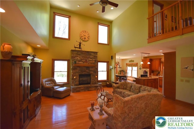living room featuring a ceiling fan, high vaulted ceiling, a stone fireplace, and wood finished floors