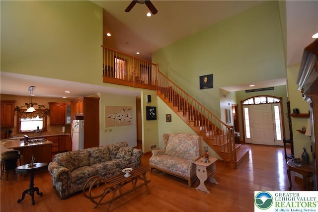 living area featuring a ceiling fan, a high ceiling, wood finished floors, and stairway