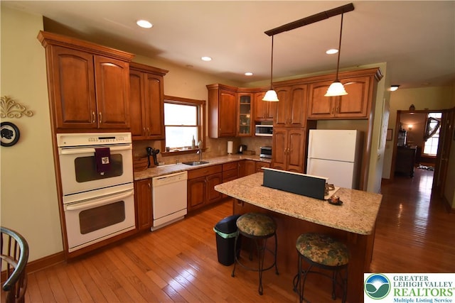 kitchen with brown cabinetry, white appliances, a kitchen breakfast bar, light wood-type flooring, and a sink