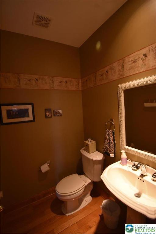 half bathroom with a sink, toilet, wood finished floors, and visible vents
