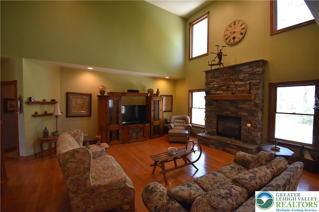 living room featuring high vaulted ceiling, baseboards, a stone fireplace, and wood finished floors