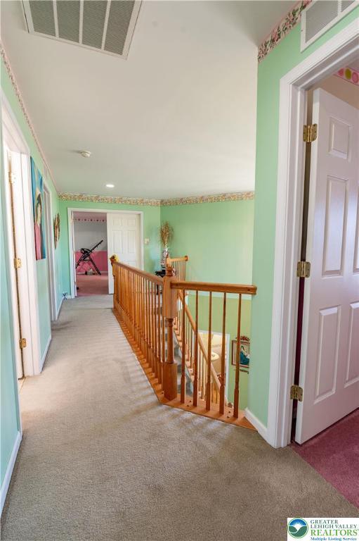 hallway with carpet floors, baseboards, visible vents, and an upstairs landing