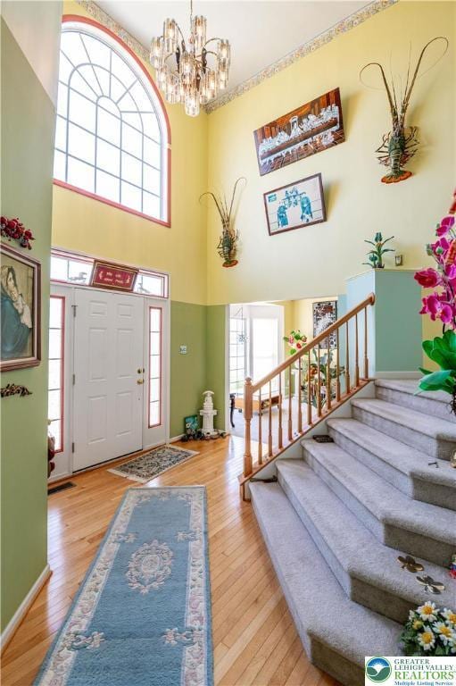 foyer entrance with wood-type flooring, a chandelier, stairway, and a towering ceiling