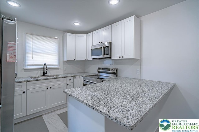 kitchen with a sink, a peninsula, stainless steel appliances, recessed lighting, and white cabinetry