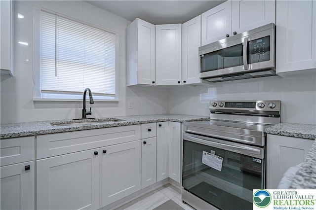 kitchen with a sink, light stone countertops, stainless steel appliances, and white cabinetry