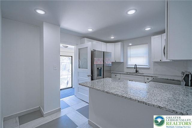kitchen with a peninsula, white cabinets, light stone counters, a sink, and appliances with stainless steel finishes