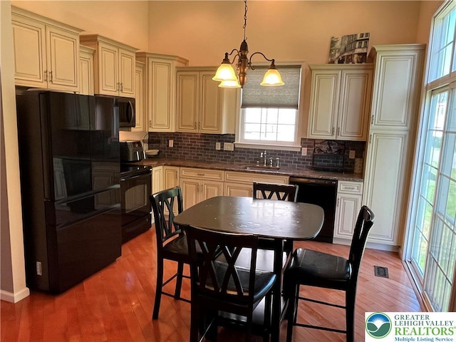 kitchen with light wood-style floors, a chandelier, a sink, backsplash, and black appliances