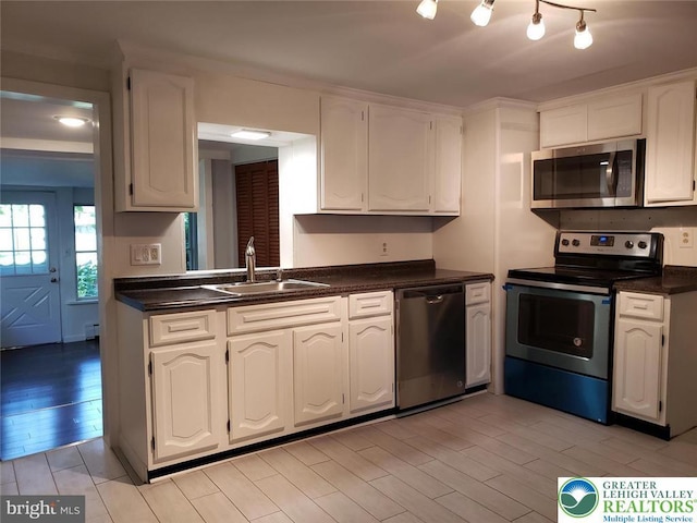 kitchen featuring dark countertops, appliances with stainless steel finishes, a sink, light wood finished floors, and white cabinetry
