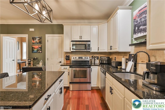 kitchen with appliances with stainless steel finishes, tasteful backsplash, a chandelier, ornamental molding, and dark wood-type flooring