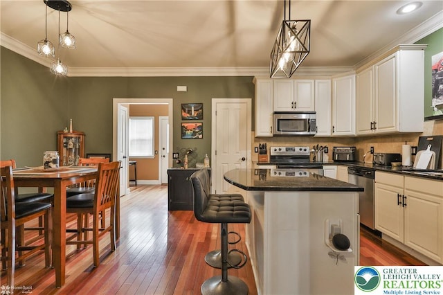kitchen with ornamental molding, a kitchen island, a kitchen breakfast bar, dark wood finished floors, and appliances with stainless steel finishes