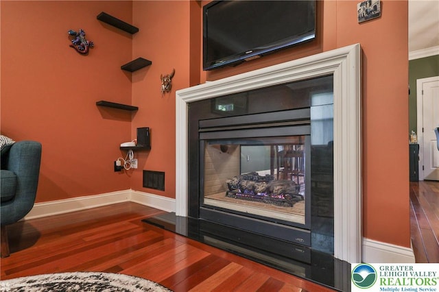 room details featuring crown molding, a multi sided fireplace, baseboards, wood finished floors, and visible vents