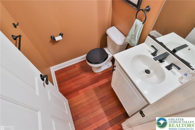 half bath with vanity, baseboards, toilet, and wood finished floors