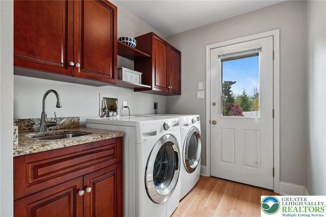 washroom with a sink, cabinet space, washer and dryer, and light wood-style flooring