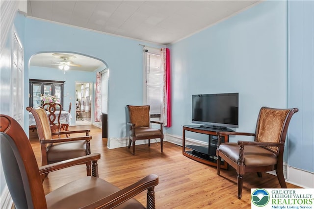 sitting room with arched walkways, ornamental molding, and light wood-style flooring